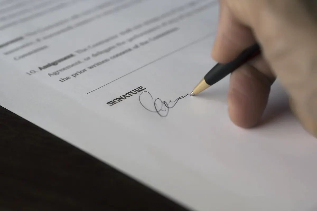 Una mano firma un documento sobre un escritorio